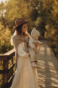 a woman holding a baby while standing on a wooden bridge next to trees and bushes