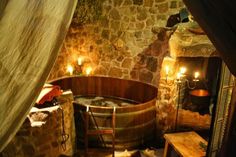 an old fashioned hot tub in a stone walled room with candles on the walls and wood floors