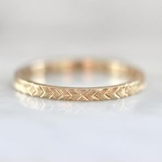 a gold wedding band with an arrow pattern on the front and side, sitting on a white surface