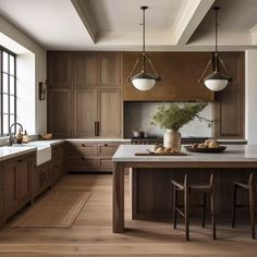 a large kitchen with wooden cabinets and an island in front of the sink is lit by two pendant lights