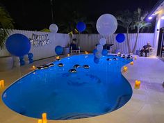 a pool with balloons and candles in the shape of dolphins is lit up at night