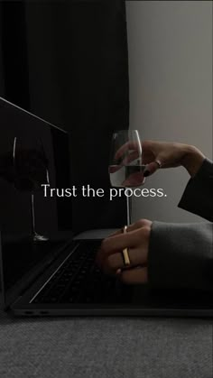 a person holding a wine glass in front of a laptop with the words trust the process