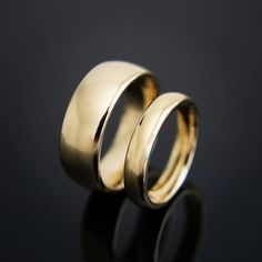 two gold wedding rings sitting on top of a black surface with one ring in the middle