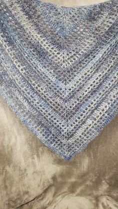 a blue crocheted shawl sitting on top of a brown velvet pillow covered in a blanket