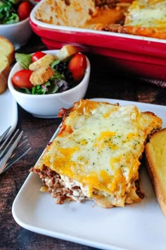 lasagna casserole on a plate with bread and salad in the background