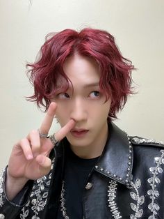 a young man with red hair and piercings making the peace sign while wearing a leather jacket