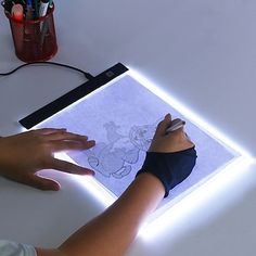 a person drawing on a piece of paper with light coming from the top and below