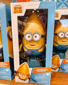 three yellow and blue toy minion figures in boxes on display at storefront window