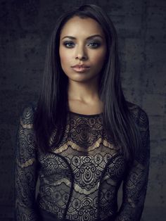 a woman with long hair wearing a black lace dress and posing for a photo in front of a brick wall