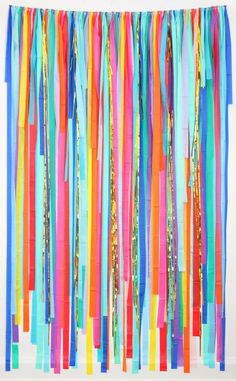 colorful streamers hanging from the ceiling in front of a white wall with gold and blue confetti