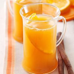 two mugs filled with orange juice and cinnamon sticks