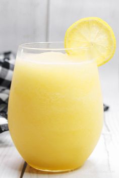 a glass filled with yellow liquid next to a slice of lemon