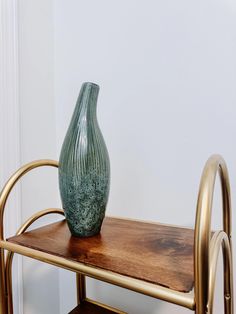 a green vase sitting on top of a wooden table next to a metal frame shelf