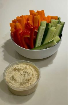 a white bowl filled with cucumbers and carrots next to a container of dip