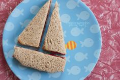 two sandwiches cut in half on a blue plate with pink and yellow fish design paper