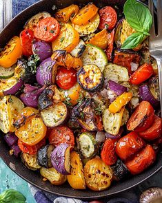 a skillet filled with roasted vegetables on top of a blue towel next to garlic