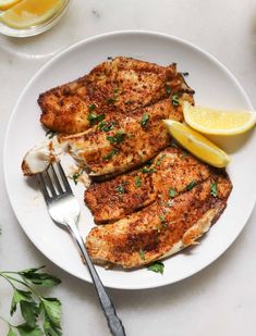 two pieces of chicken on a white plate with lemon wedges and parsley next to it