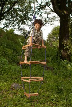 a young boy climbing on a ladder made out of wood and rope, in the woods