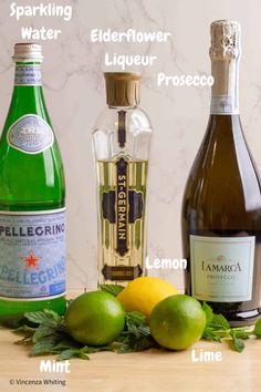 three different types of alcohol on a table with lemons, limes and water