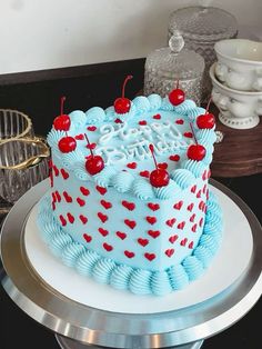 a blue and red birthday cake with cherries on the top sitting on a silver platter