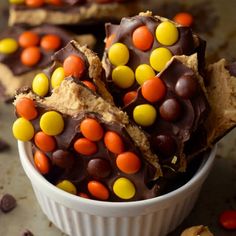 a white bowl filled with chocolate candy bars and candy candies next to a spoon