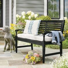 a black bench sitting on top of a patio next to flowers and a dog in the background