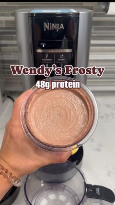 a person holding a cup in front of a blender with the words wendy's frosty on it