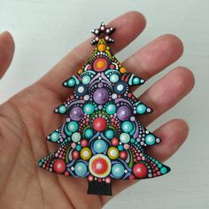 a hand holding a colorful christmas tree brooch