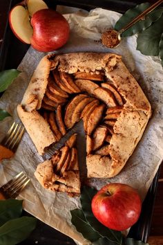 an apple pie with one slice cut out and apples on the side next to it