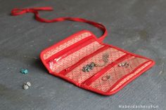 a red purse with several pairs of earrings on the floor next to some silver beads