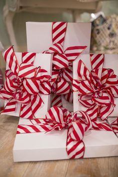 two white boxes with red and white striped bows on top of each box, sitting on a wooden table