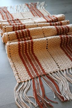 three pieces of crocheted fabric with fringes on top of each other, sitting on a wooden floor