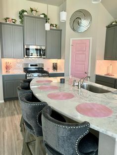 a kitchen with grey cabinets and pink accents on the countertop, along with gray stools