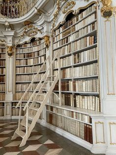 an old library filled with lots of books next to a spiral stair case and chandelier