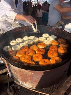 some food is being cooked in a large pan on the grill with other people around