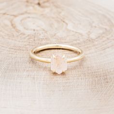 a close up of a gold ring with a white stone in the center on a wooden surface