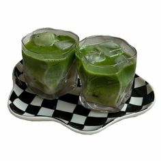 two glasses filled with green liquid on top of a checkered plate