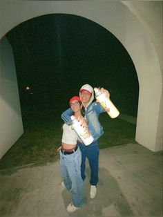 two people are posing with skateboards in front of an arch at night time,