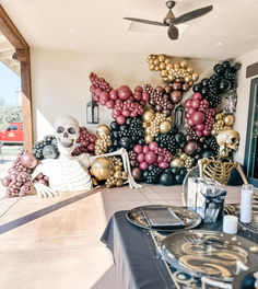 there is a skeleton sitting on the table in front of some balloons that look like skulls