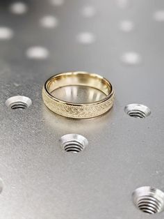 two gold wedding rings sitting on top of a metal surface with rivets around them