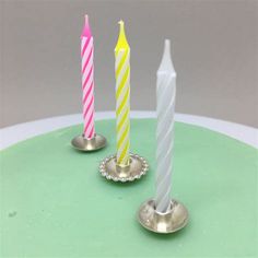 three candles are sitting on top of a green cake with two silver dishes and one pink candle