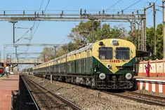 a yellow and green train traveling down tracks next to a platform with people walking on the side