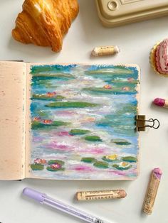 an open notebook with water lilies and croissants next to it on a table