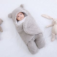 a baby in a bunny costume laying next to two stuffed animals on a white blanket