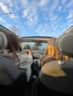 two women sitting in the back seat of a car looking out at the ocean and blue sky