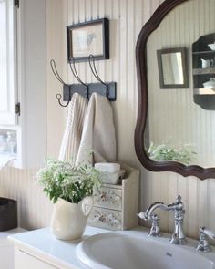 a bathroom sink sitting under a mirror next to a white counter top with flowers on it