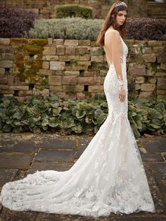 a woman in a white wedding dress standing on a brick walkway with her back to the camera