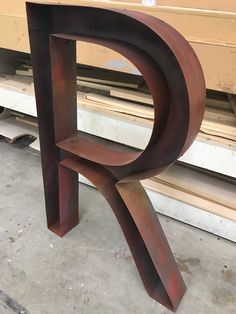 a large metal letter sitting on top of a wooden table next to a pile of wood planks