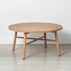 a round wooden table sitting on top of a hard wood floor next to a white wall