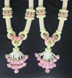 two necklaces with pink flowers and green beads hanging from the sides on a black background